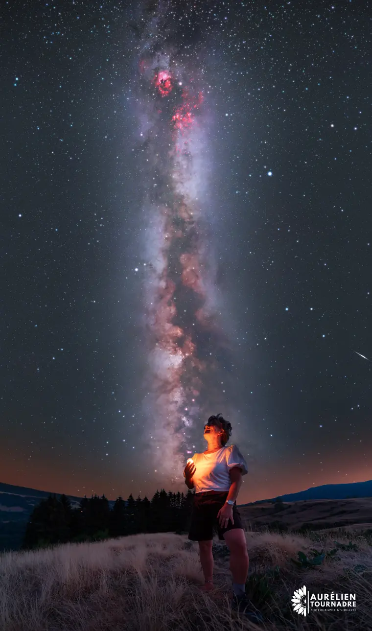 La Voie lactée déployée dans le ciel d'une nuit d'été, au-dessus d'une crête herbeuse où une femme lève les yeux vers les étoiles
